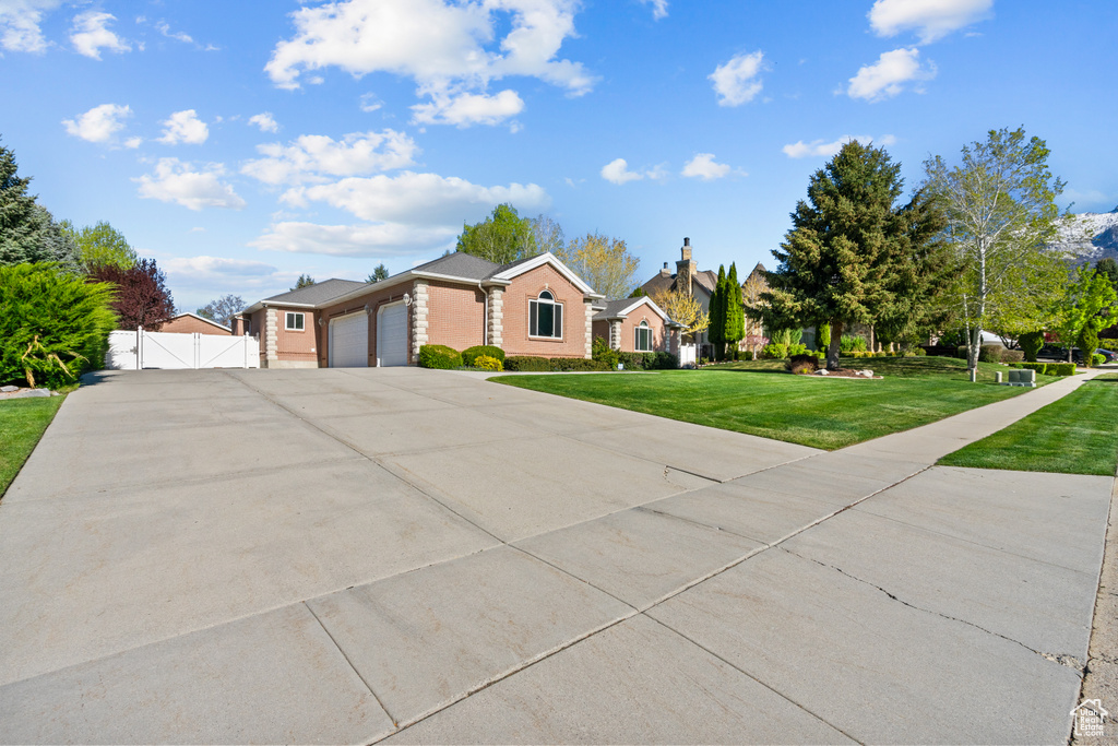 Ranch-style house featuring driveway, a gate, fence, a front lawn, and an attached garage