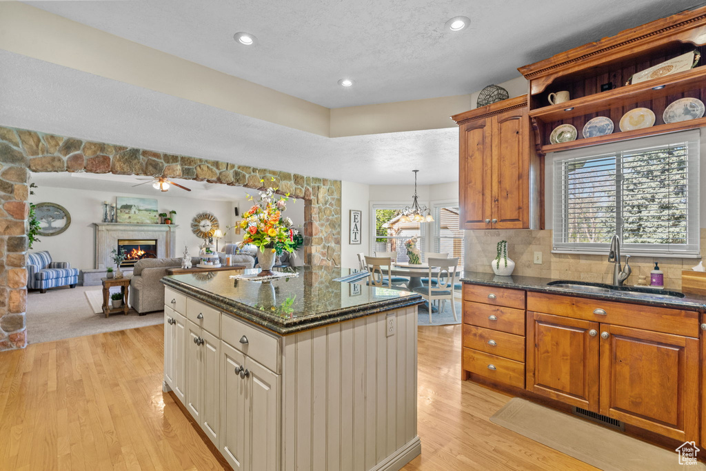Kitchen with a sink, a glass covered fireplace, dark stone counters, light wood-type flooring, and a kitchen island