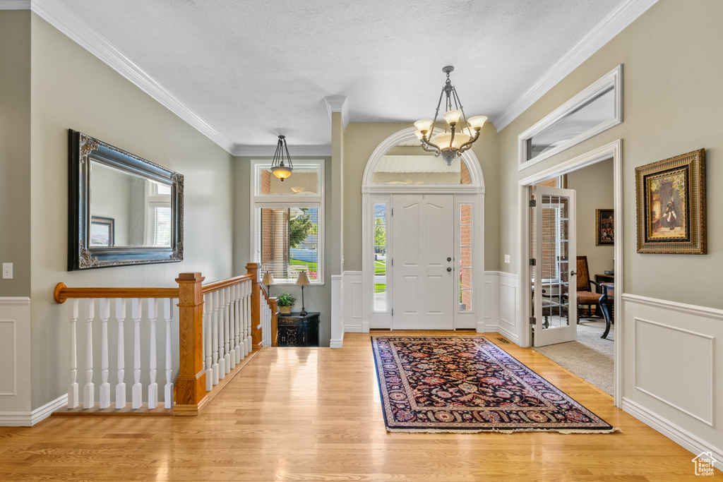 Foyer entrance featuring a healthy amount of sunlight, crown molding, wood finished floors, and a chandelier