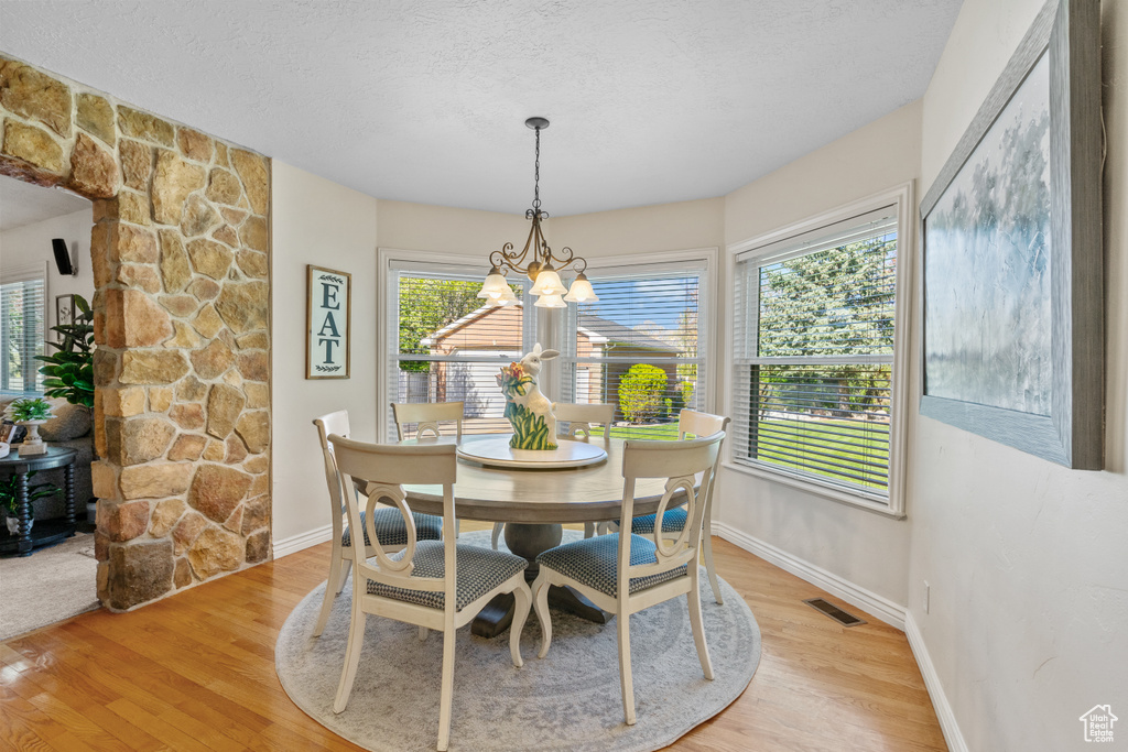 Dining area with a textured ceiling, visible vents, baseboards, a notable chandelier, and light wood-style floors