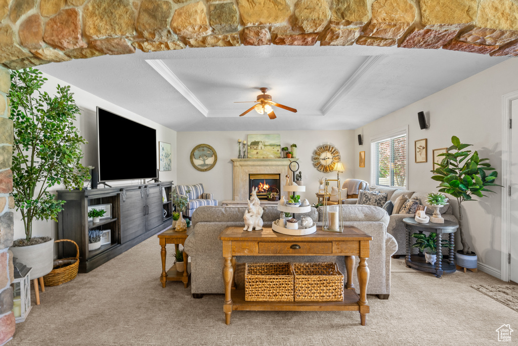 Living area with carpet flooring, a ceiling fan, a glass covered fireplace, and a raised ceiling
