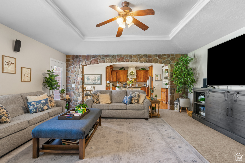 Living room with crown molding, a ceiling fan, a tray ceiling, and light colored carpet