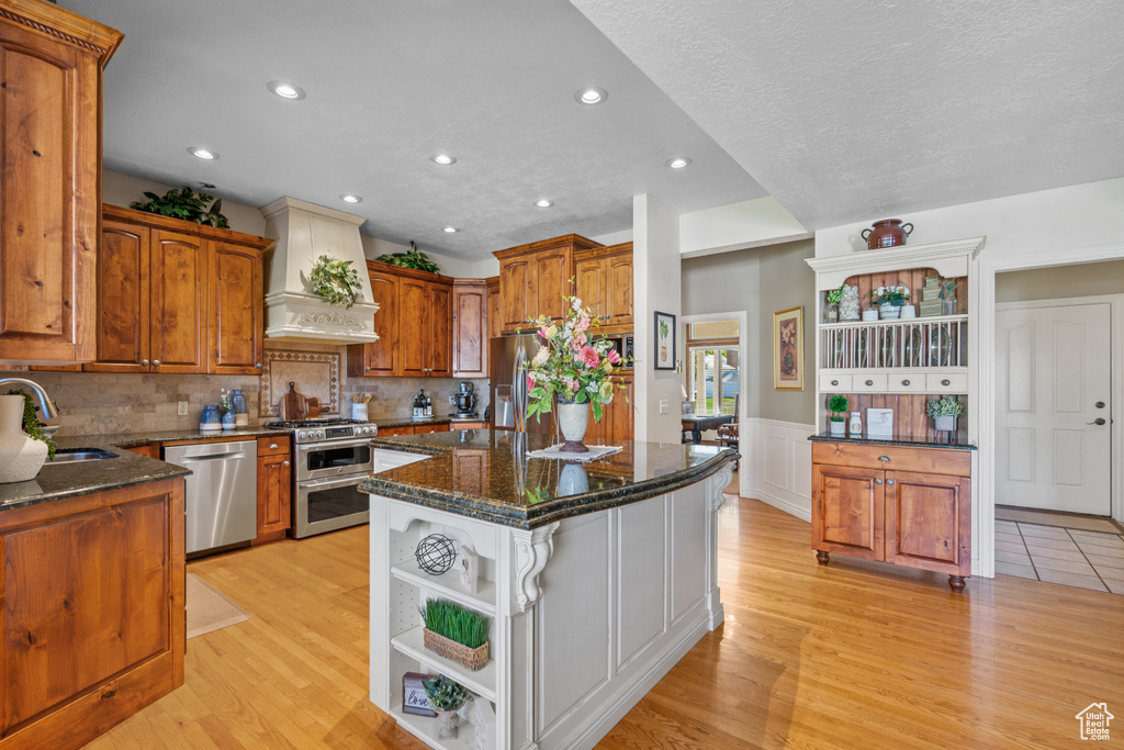 Kitchen featuring open shelves, custom exhaust hood, dark stone counters, a sink, and stainless steel appliances