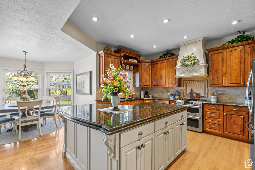 Kitchen featuring a kitchen island, stainless steel appliances, light wood finished floors, and custom range hood
