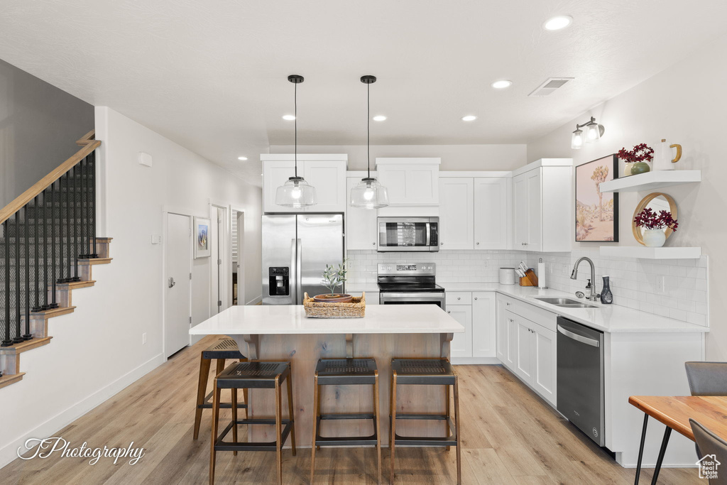 Kitchen featuring a sink, open shelves, white cabinetry, decorative backsplash, and appliances with stainless steel finishes