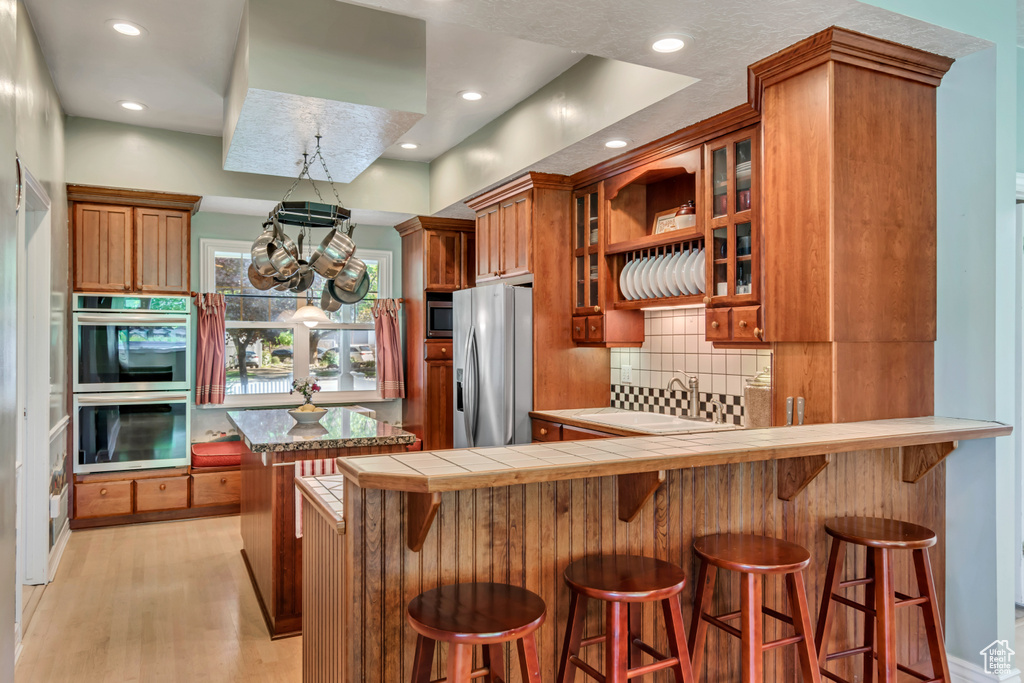 Kitchen with brown cabinetry, stainless steel appliances, tasteful backsplash, and glass insert cabinets