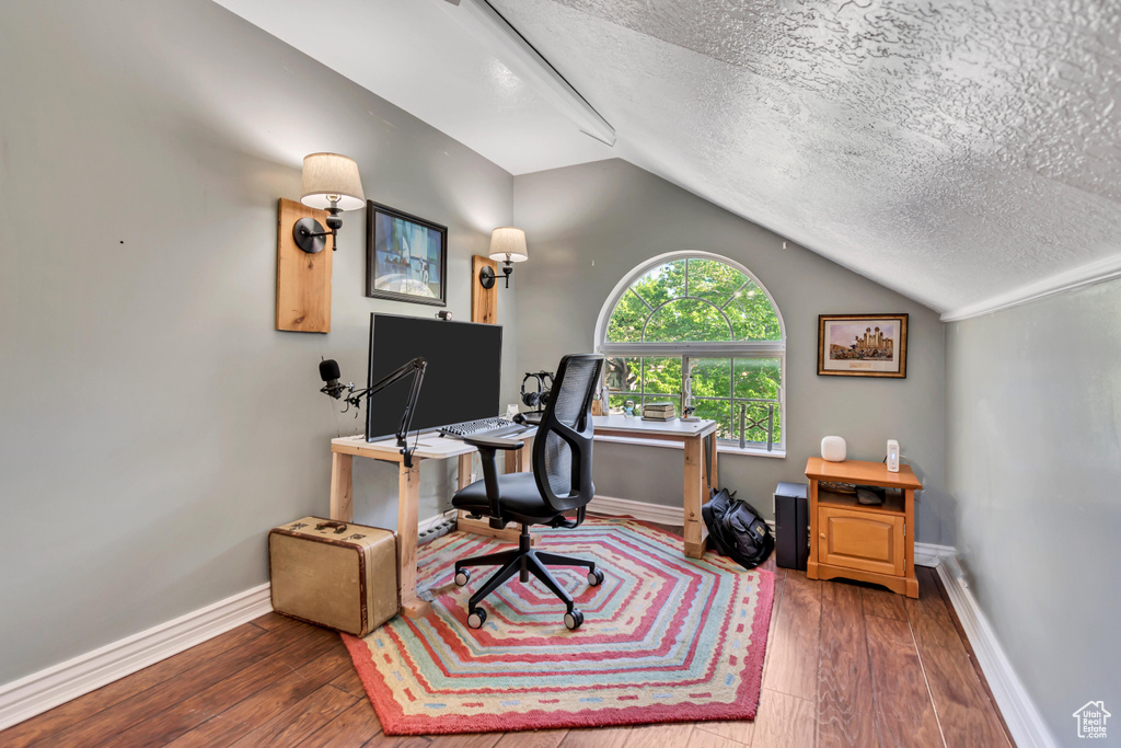 Office area with baseboards, wood-type flooring, a textured ceiling, and vaulted ceiling
