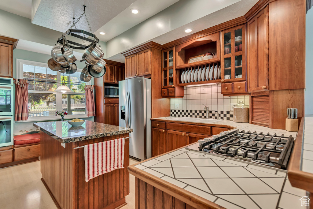 Kitchen featuring brown cabinetry, tile counters, backsplash, appliances with stainless steel finishes, and recessed lighting