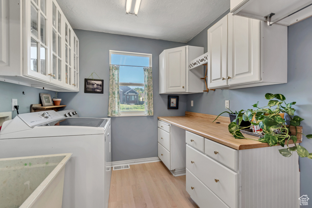 Laundry area featuring washing machine and dryer, cabinet space, light wood-type flooring, visible vents, and baseboards
