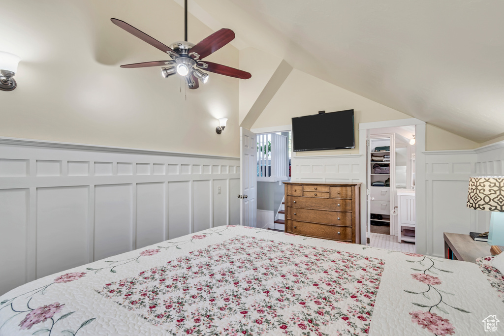 Bedroom featuring a wainscoted wall, a decorative wall, lofted ceiling, and ceiling fan