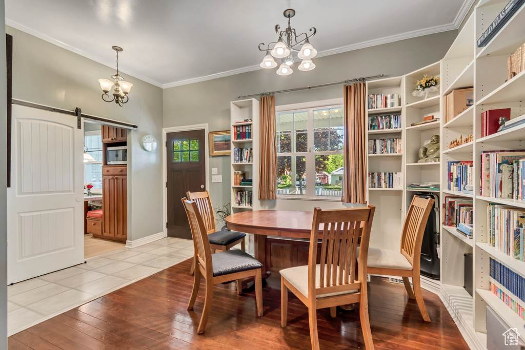 Dining area with a barn door, baseboards, ornamental molding, a chandelier, and hardwood / wood-style floors