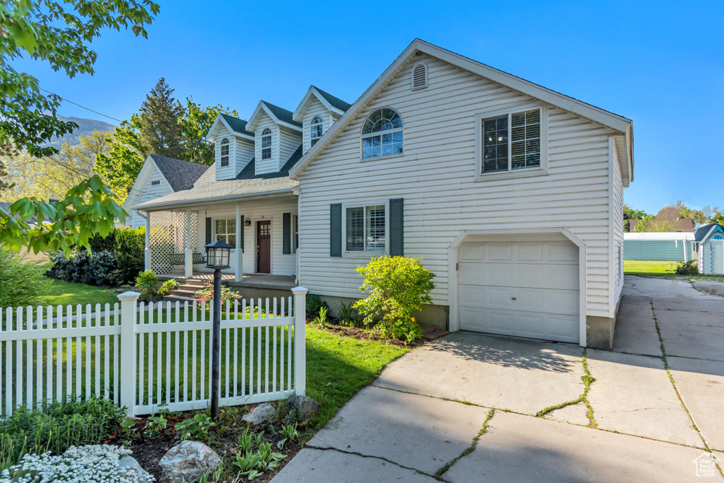 Cape cod home with covered porch, concrete driveway, a garage, a front yard, and a fenced front yard