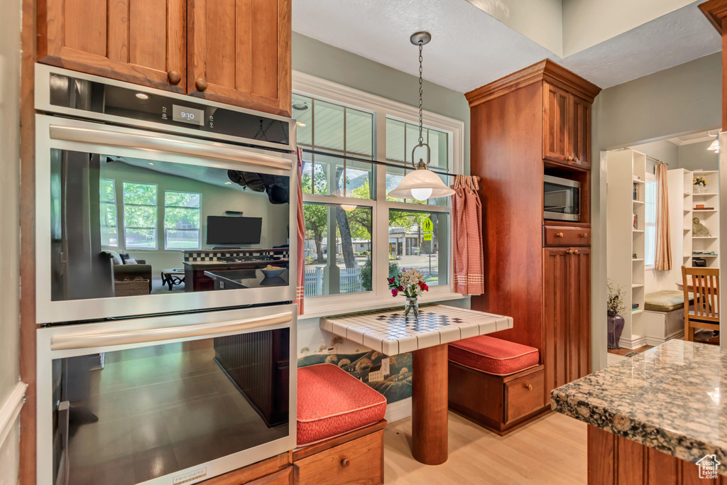 Kitchen with light wood-style floors, brown cabinets, hanging light fixtures, and appliances with stainless steel finishes