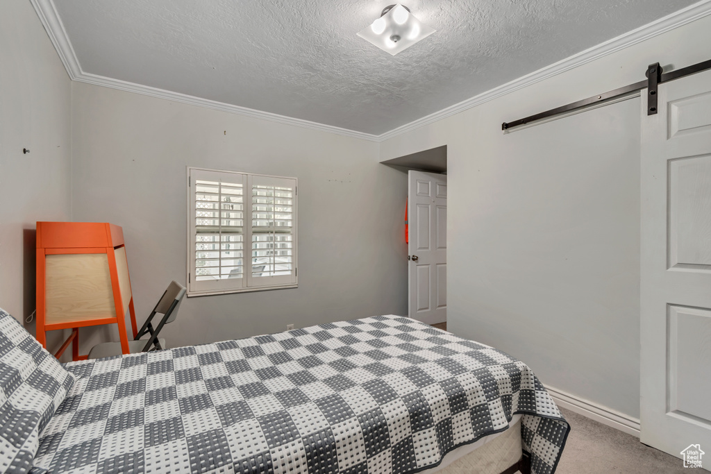 Carpeted bedroom featuring crown molding, a textured ceiling, and a barn door