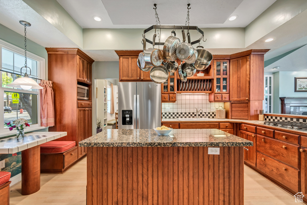 Kitchen with stainless steel appliances, brown cabinetry, light wood-type flooring, a kitchen island, and tasteful backsplash