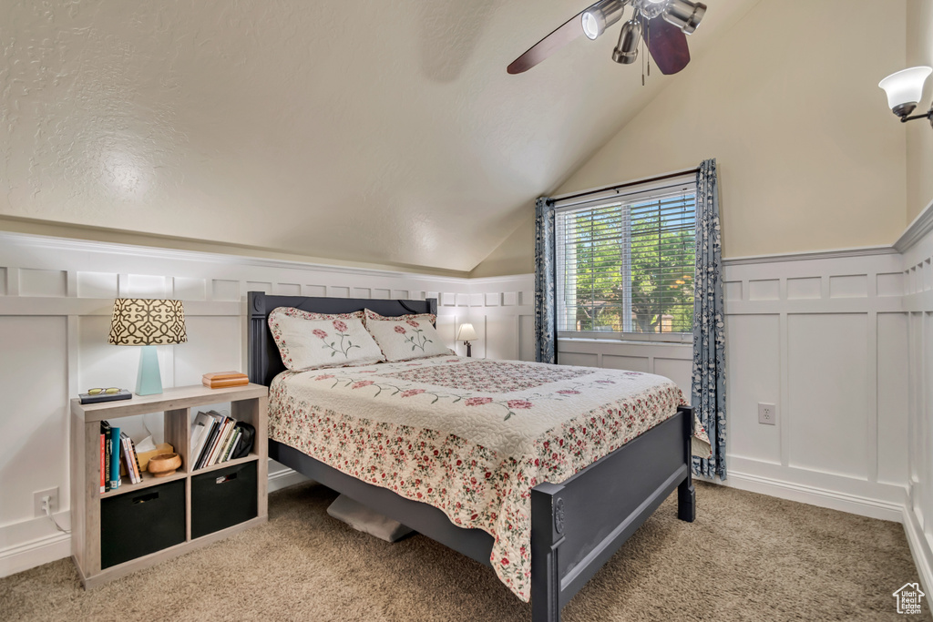 Bedroom with a ceiling fan, a decorative wall, carpet, and vaulted ceiling