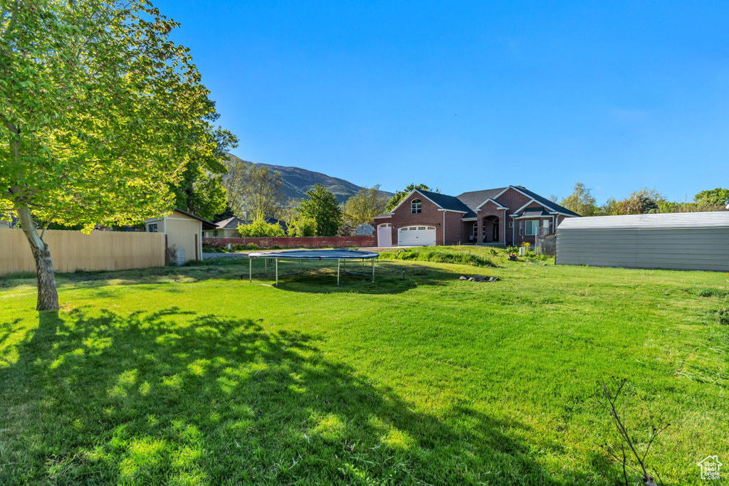 View of yard featuring an outbuilding, a mountain view, fence, a trampoline, and a storage shed