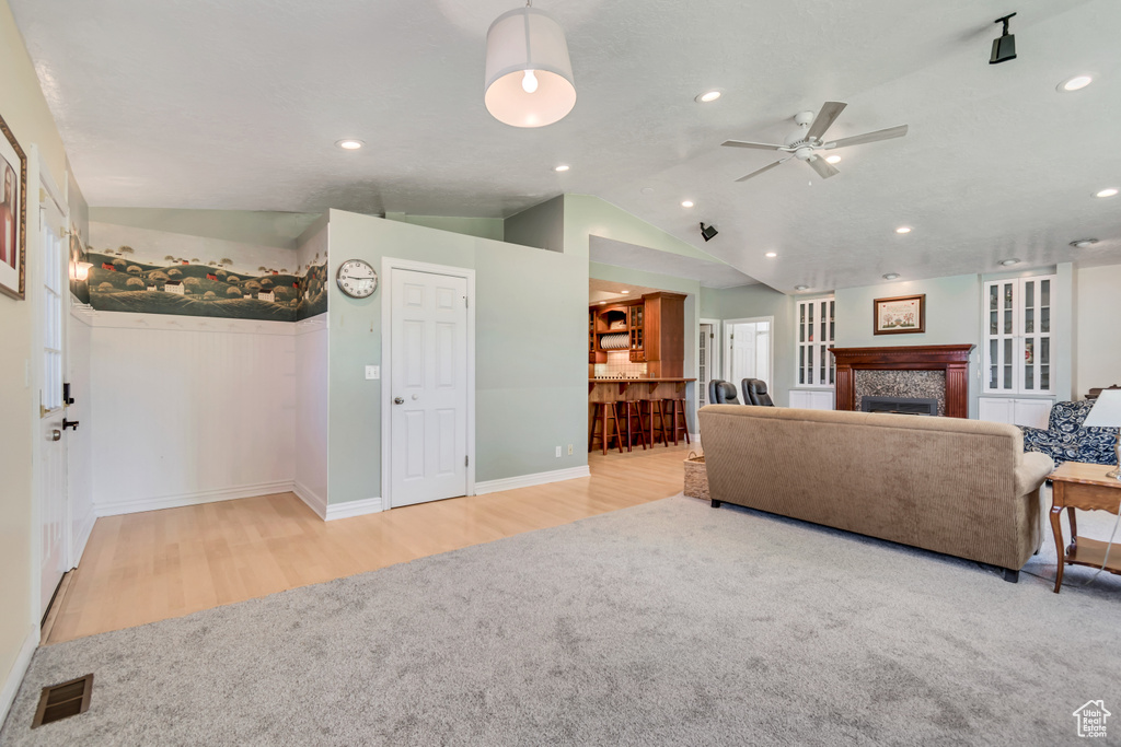 Living room with a ceiling fan, visible vents, vaulted ceiling, a tile fireplace, and wood finished floors