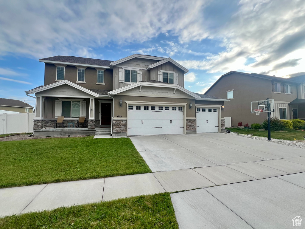 Craftsman inspired home with covered porch, a front lawn, stone siding, and driveway