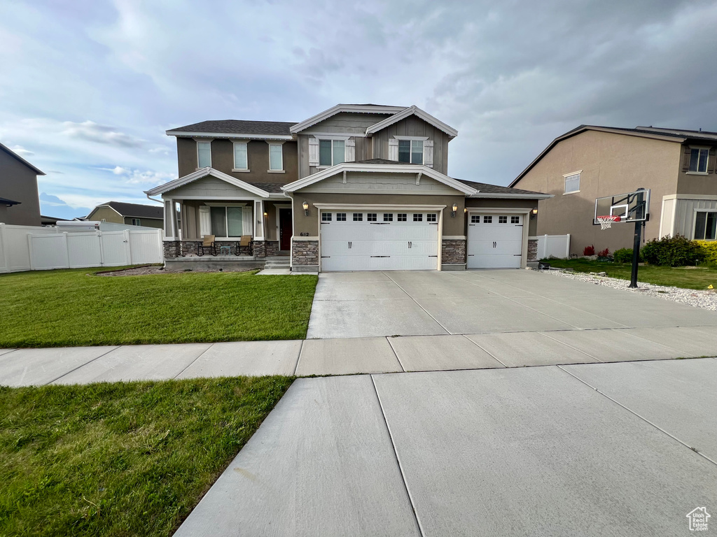 Craftsman house featuring stone siding, a garage, fence, concrete driveway, and a front lawn