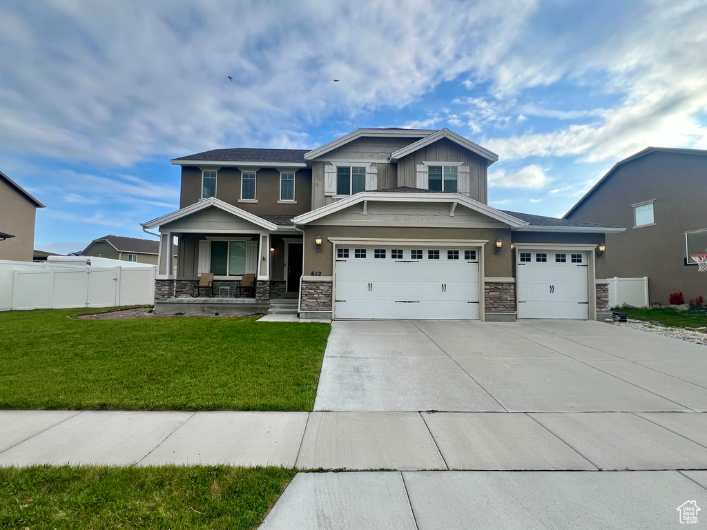 Craftsman-style house with a porch, fence, stone siding, concrete driveway, and a front yard
