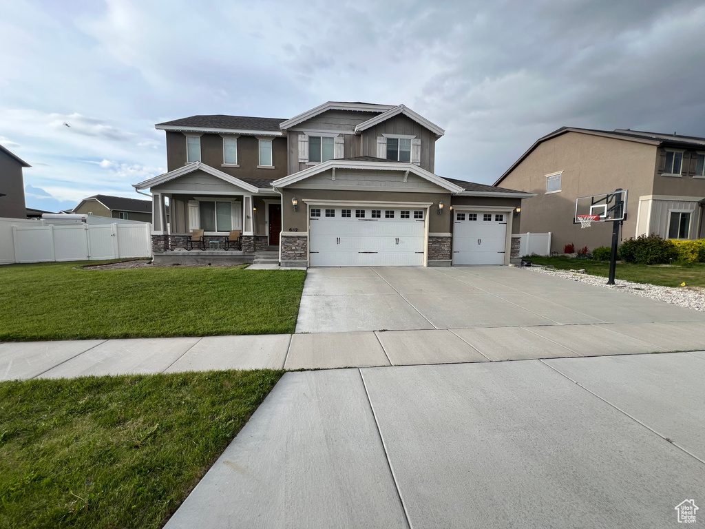 Craftsman house featuring fence, stone siding, concrete driveway, a garage, and a front lawn