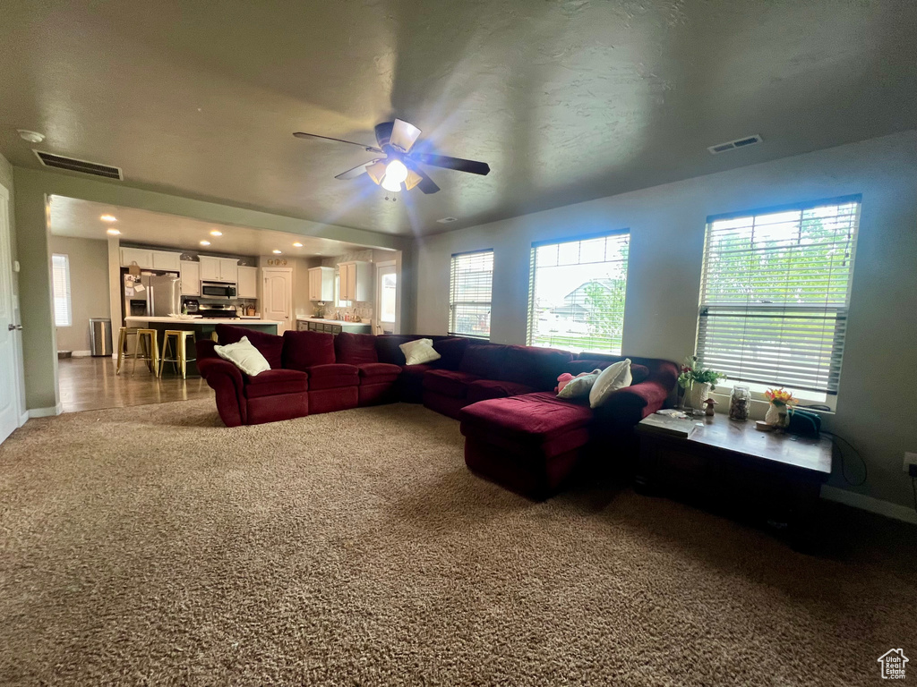 Living area featuring carpet flooring, visible vents, baseboards, and a ceiling fan
