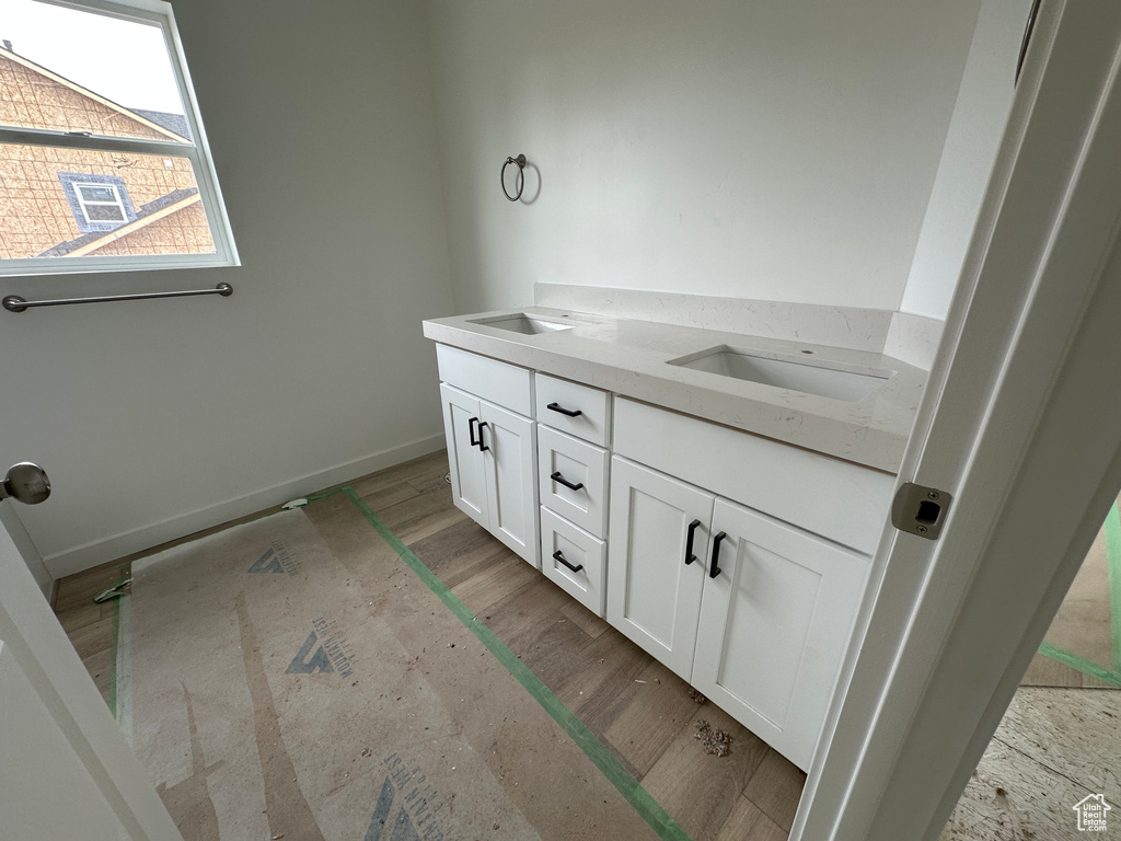Full bath featuring baseboards, double vanity, a sink, and wood finished floors