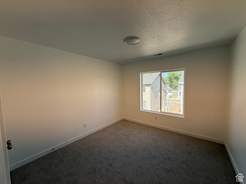 Unfurnished room with dark colored carpet and a textured ceiling