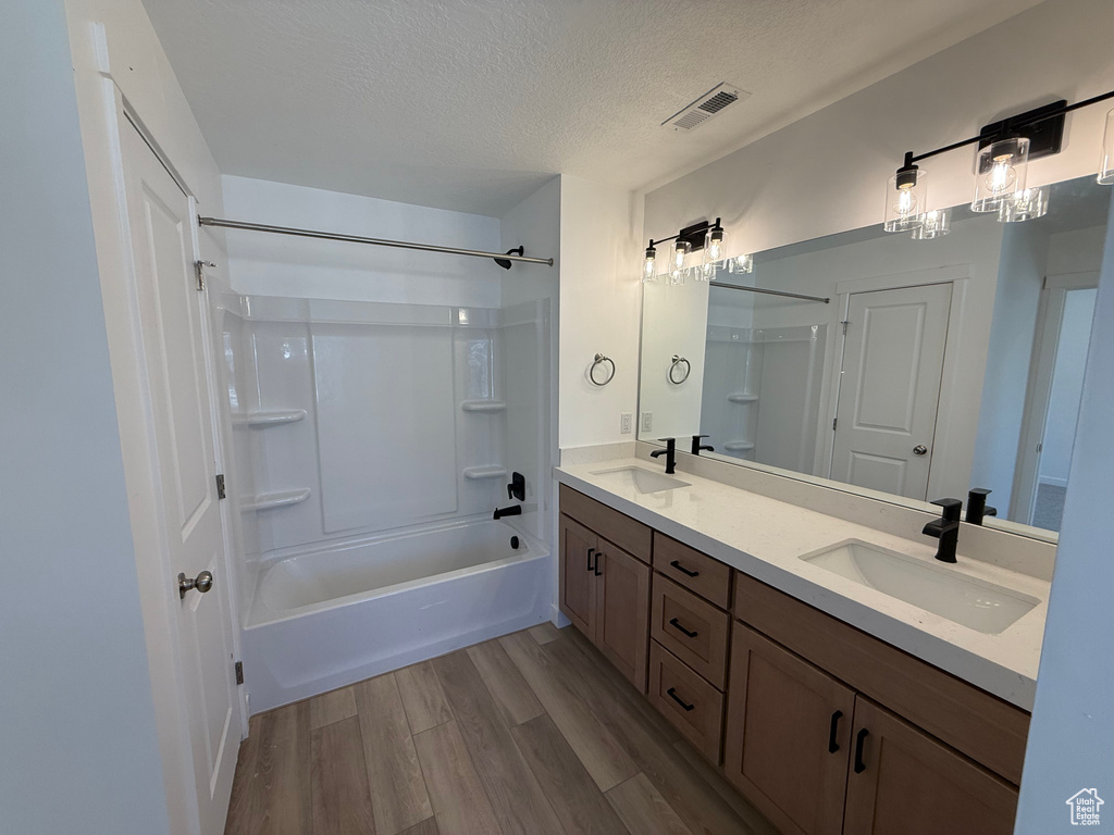Full bath with double vanity, wood finished floors, shower / washtub combination, and a textured ceiling