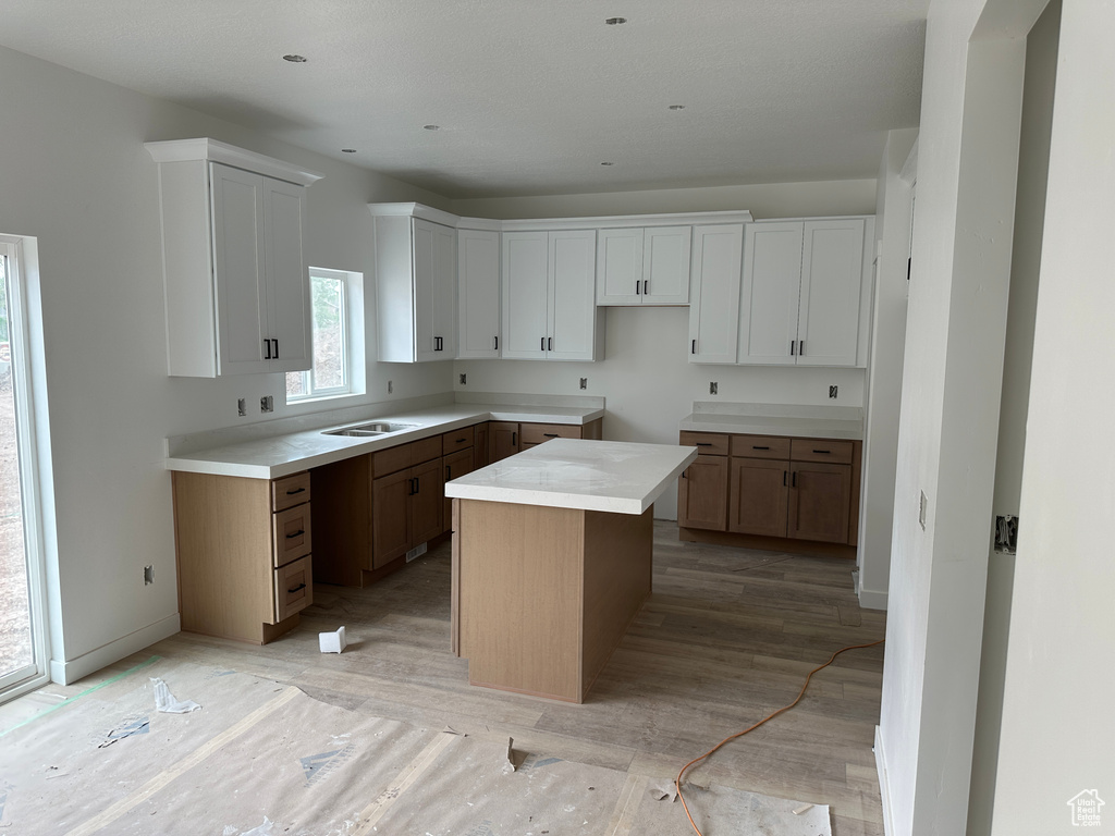 Kitchen with a sink, white cabinetry, a kitchen island, and light wood-style floors
