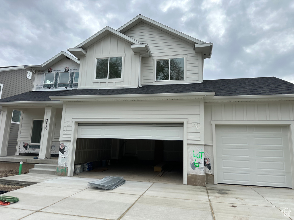 View of front of home with board and batten siding, an attached garage, a shingled roof, and driveway