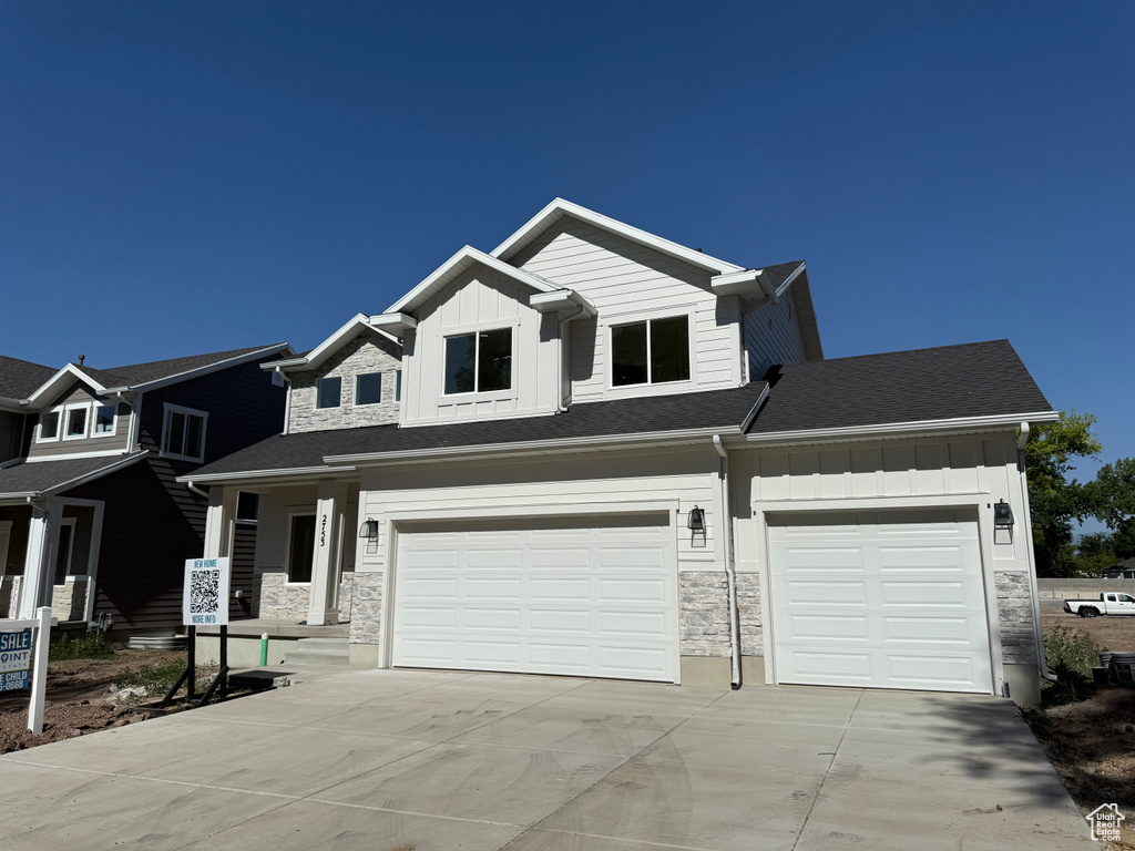View of front facade with board and batten siding, concrete driveway, an attached garage, and stone siding