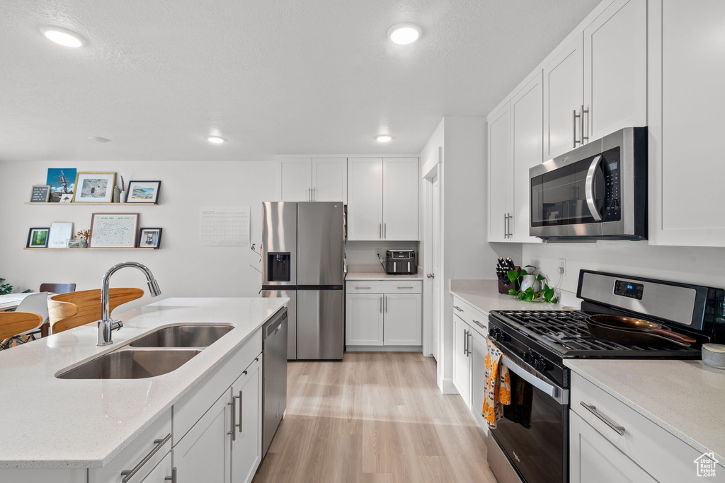 Kitchen with a sink, a center island with sink, light wood finished floors, white cabinetry, and appliances with stainless steel finishes