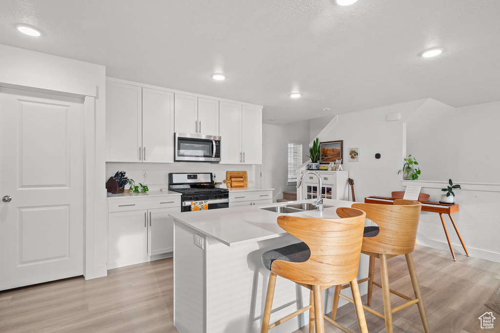 Kitchen with a sink, a kitchen bar, white cabinetry, stainless steel appliances, and light wood-type flooring