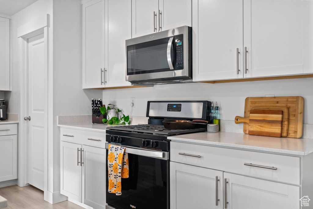 Kitchen with light wood finished floors, white cabinets, and appliances with stainless steel finishes