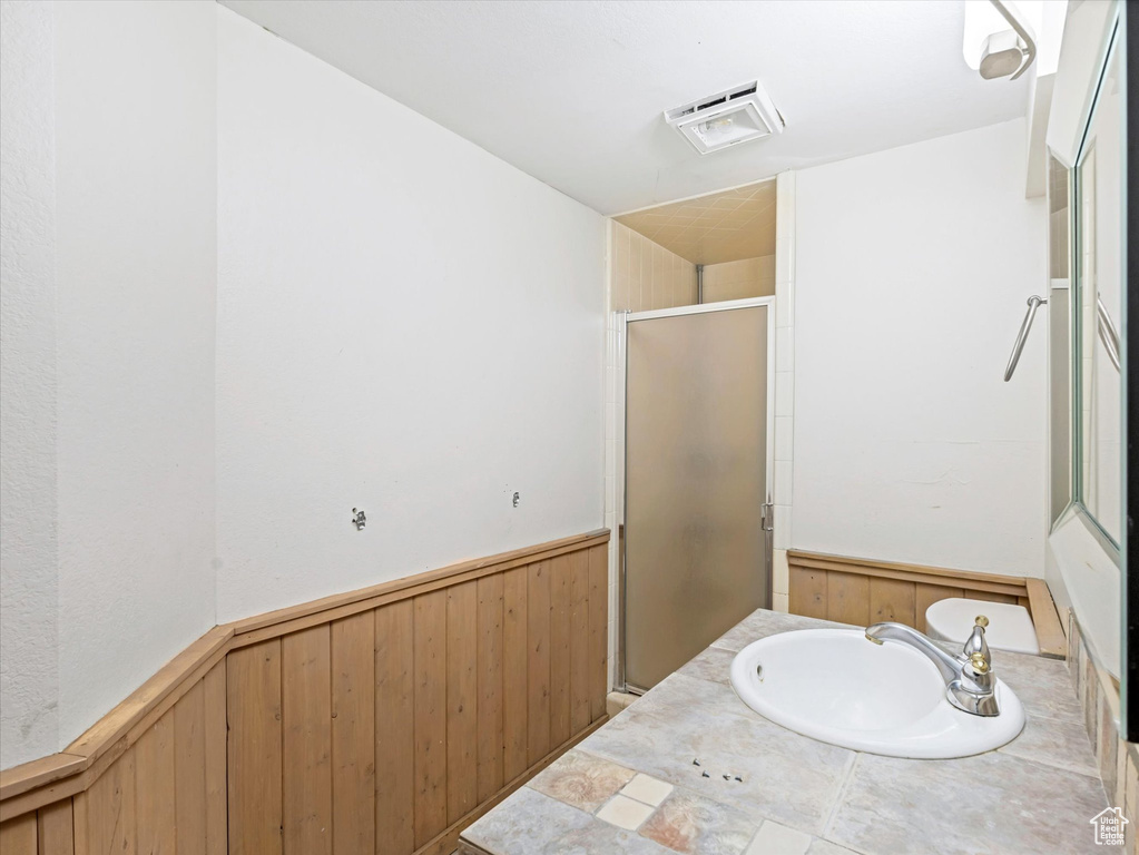 Bathroom with a stall shower, a sink, a wainscoted wall, visible vents, and wood walls