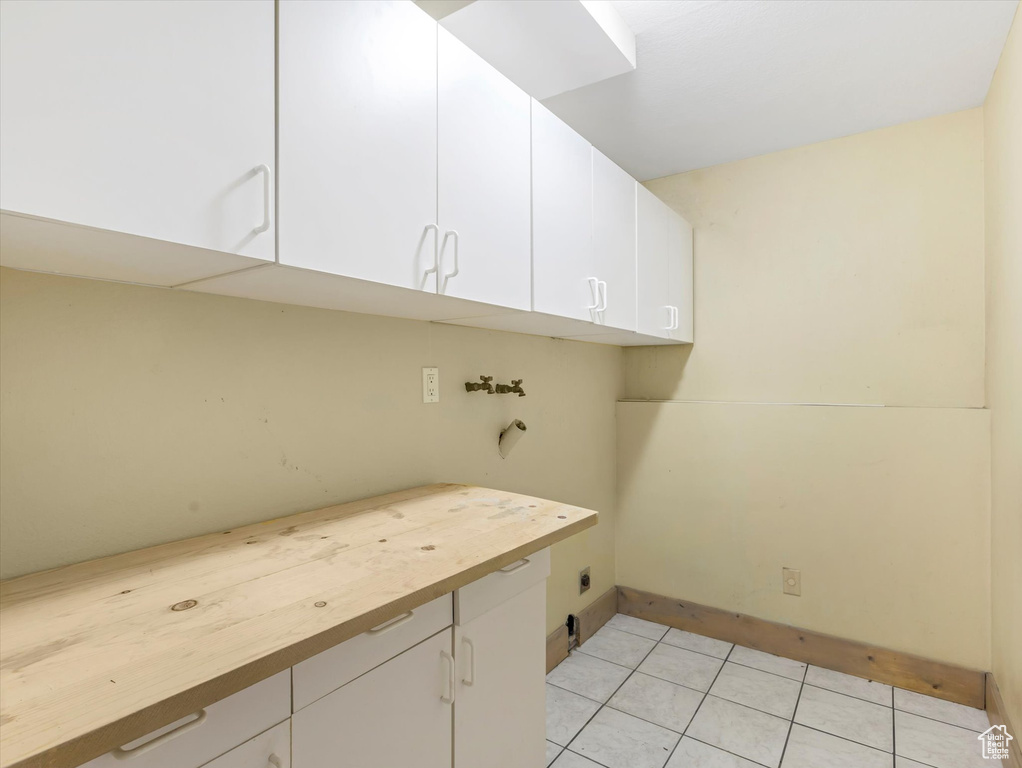 Washroom featuring light tile patterned floors, electric dryer hookup, cabinet space, washer hookup, and baseboards
