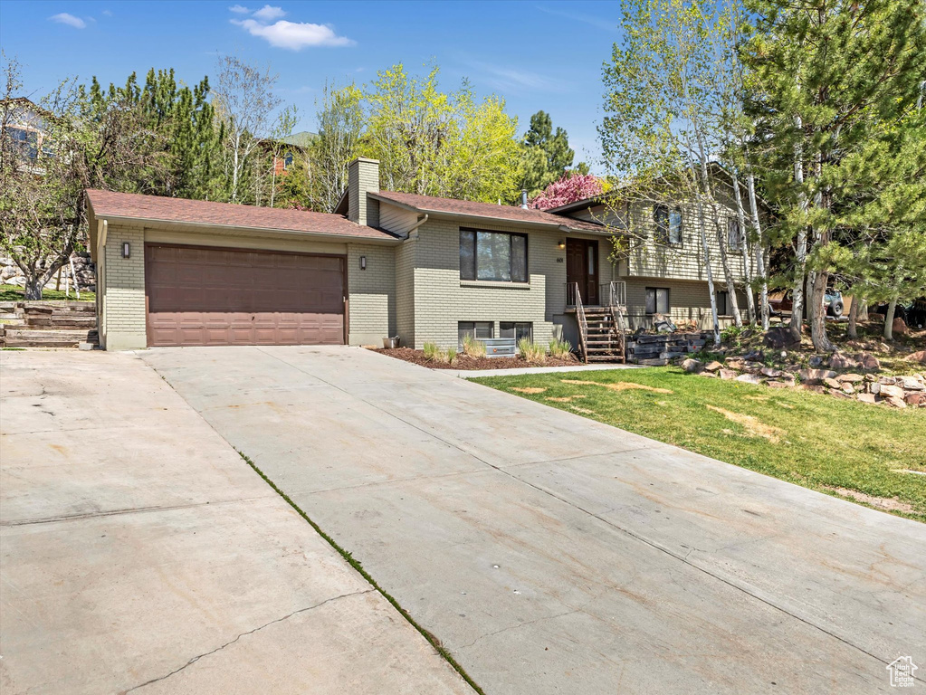 Tri-level home featuring a chimney, brick siding, a garage, concrete driveway, and a front yard