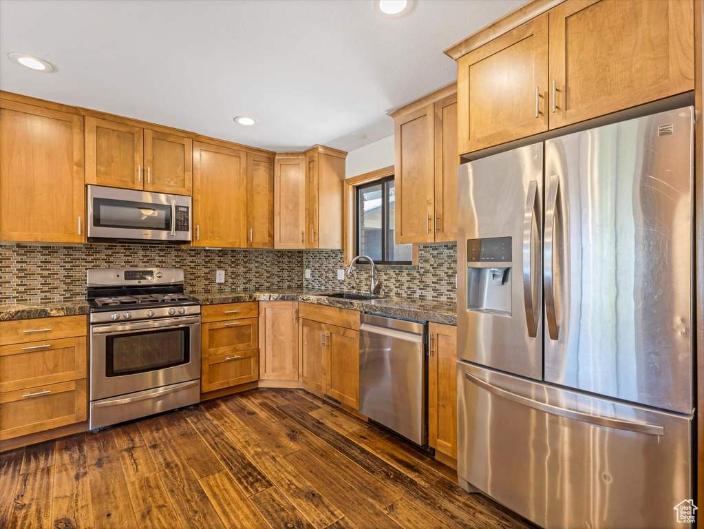 Kitchen with recessed lighting, a sink, decorative backsplash, dark wood-type flooring, and appliances with stainless steel finishes