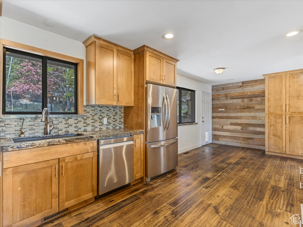 Kitchen with a sink, dark stone countertops, dark wood-type flooring, backsplash, and appliances with stainless steel finishes