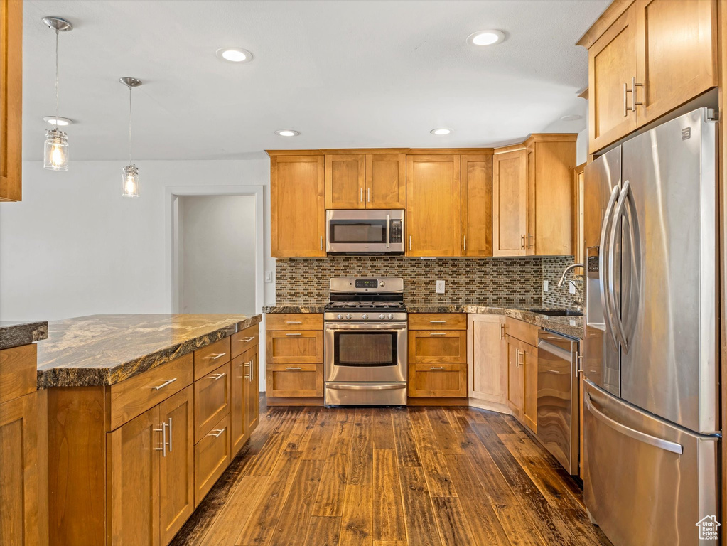 Kitchen with dark wood-style flooring, a sink, brown cabinets, stainless steel appliances, and tasteful backsplash