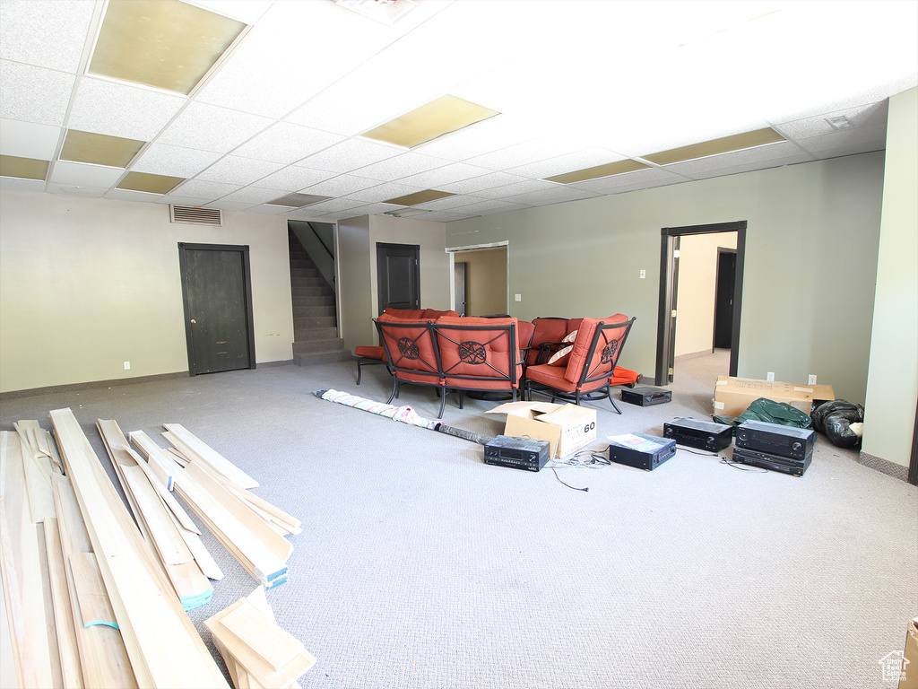 Carpeted living area featuring stairway, baseboards, visible vents, and a paneled ceiling