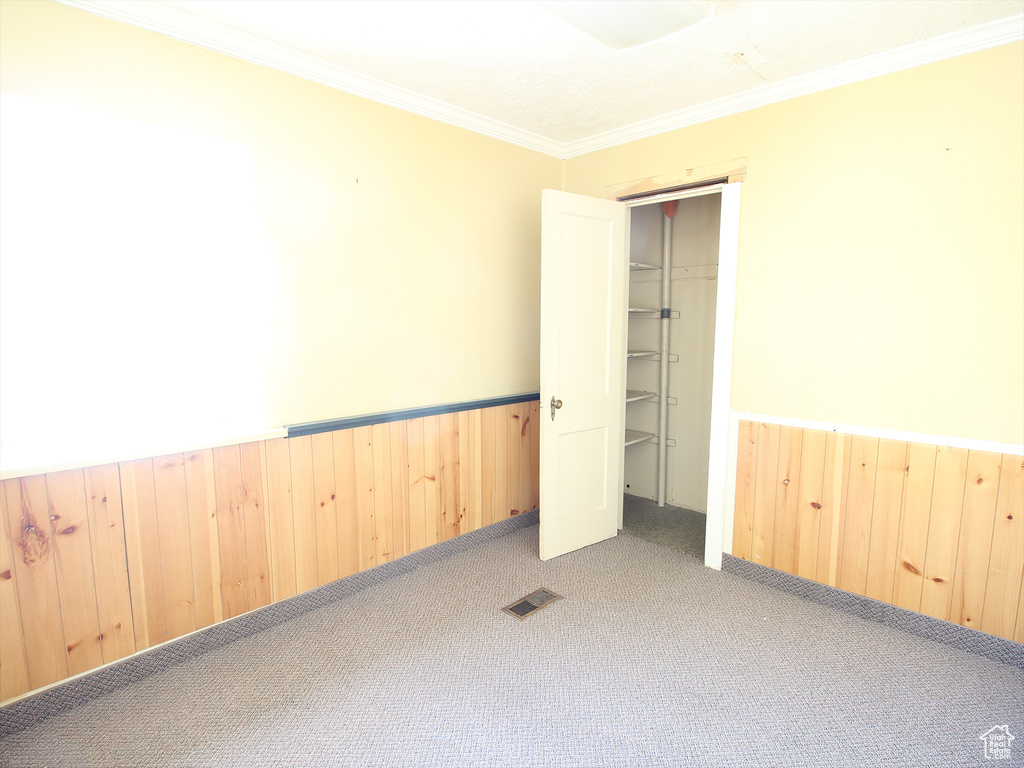 Carpeted spare room with wainscoting, crown molding, wooden walls, and visible vents