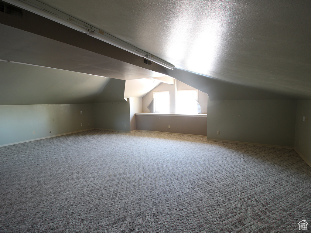 Bonus room featuring lofted ceiling, a textured ceiling, baseboards, carpet flooring, and visible vents