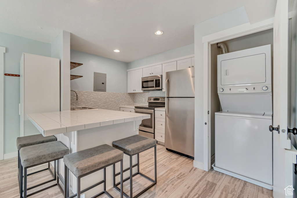 Kitchen featuring a sink, stacked washer / drying machine, a kitchen bar, tile counters, and appliances with stainless steel finishes