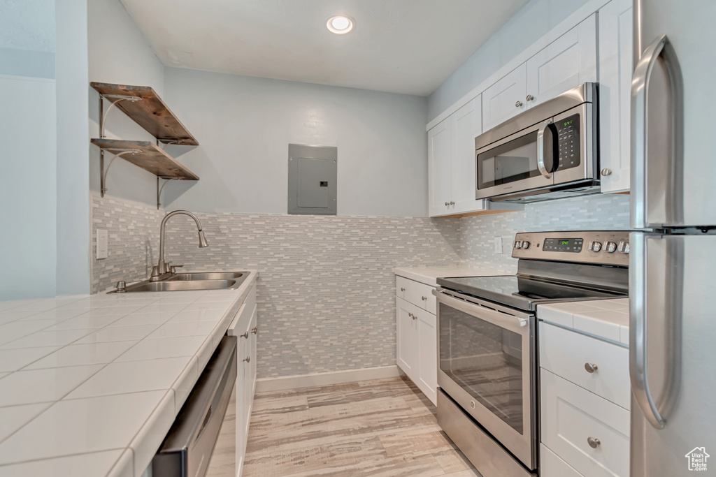 Kitchen with a sink, open shelves, stainless steel appliances, tile counters, and electric panel