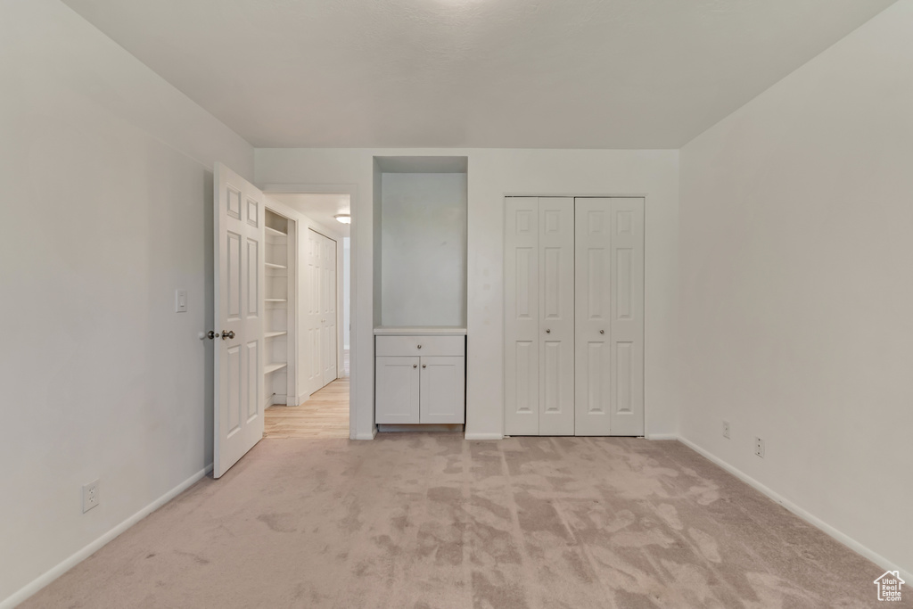 Unfurnished bedroom with baseboards, light carpet, and a closet
