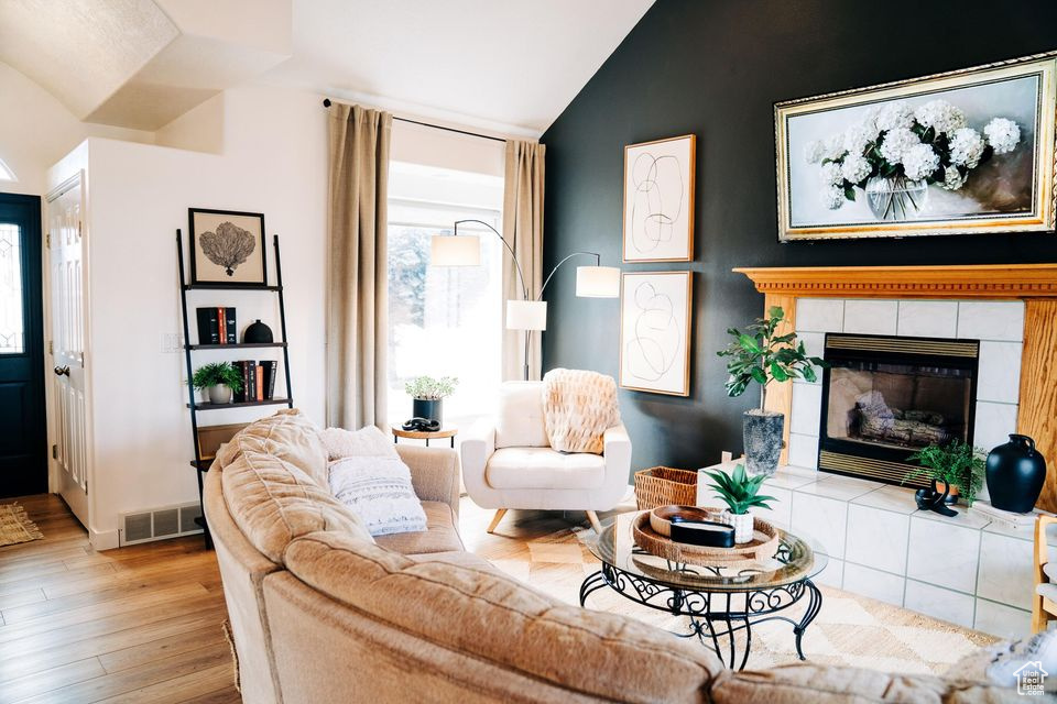 Living room featuring lofted ceiling, a tile fireplace, visible vents, and wood finished floors