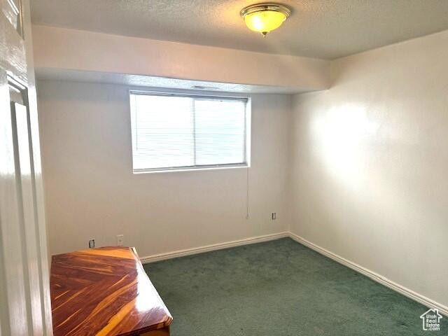 Spare room with dark colored carpet, a textured ceiling, and baseboards